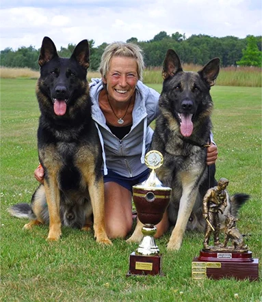 Ein Foto von Gina Meister mit ihren beiden Schäferhunden Tango und Texas an den Seiten und ihren gewonnen Pokalen